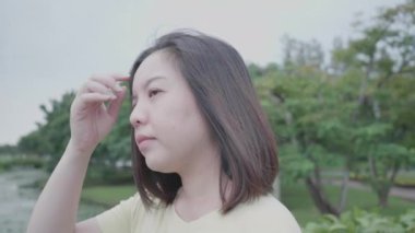 Yağmurlu havada, yumuşak, kısa saçlı, hafif rüzgarlı havada, açık hava parkında dinlenen Asyalı bir kadın. Karantina koronavirüs hastalığından sonra tatilde gevşeme sarı tişörtü