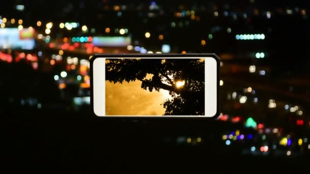 夜のモーターウェイで時間経過ぼやけた車のランプとスマートフォンでオレンジ色の夕焼け曇り空に風によって動きのあるビデオシルエットの木 忙しい営業日の中で美しい自然をコンセプト — ストック動画