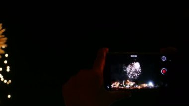 4K Smart telefon, halka açık parktaki siyah gökyüzü arka planında güzel renkli havai fişek gösterisi kaydediyor. Noel ve Yeni Yıl Festivali 'ni kutlayın. Mutlu bayram yıldönümü partisi