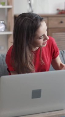 Genç bir kadın, evinde davetkar ve rahat bir çalışma alanı yaratırken dikkatle dizüstü bilgisayarına odaklanıyor.