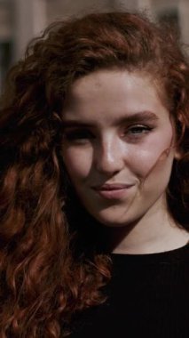 Kendine güvenen, kıvırcık saçlı, yumuşak, doğal ışığa yakalanmış genç bir kadının çarpıcı portresi..