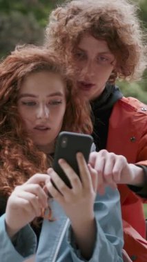 İki hevesli genç açık havada akıllı bir telefona bakarken keyifli bir an paylaşıyorlar.