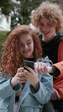Kıvırcık saçlı iki genç arkadaş, doğal ortamında akıllı bir telefonla eğleniyorlar..