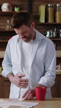 Modern bir mutfak ortamında, bir adam midesini tutarken rahatsızlık hissediyor gibi görünüyor, tedirgin görünüyor.