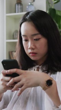 Genç bir kadın rahat ve rahat bir ev ortamının keyfini çıkarırken akıllı telefonuna derinden odaklanır.