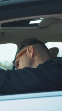 Şık gözlükler takan bir adam rahat bir şekilde arabada oturuyor ve modern bir şehir yaşam tarzının özünü sergiliyor.