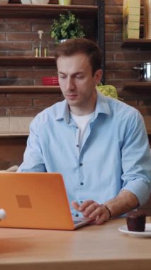 Bir adam sıcak, davetkar bir kafe ortamında dizüstü bilgisayarı üzerinde çalışmaya odaklanır.