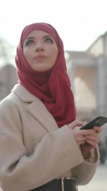 Çarpıcı kırmızı tesettür ve krem ceketli şık bir kadın, şehir ortamında modern moda eğilimlerini somutlaştırıyor.