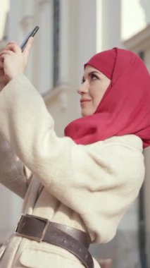 Kendine güvenen bir kadın, canlı kırmızı bir başörtüsüyle süslenir, dışarıda güneşlenirken eğlenceli bir selfie çeker.