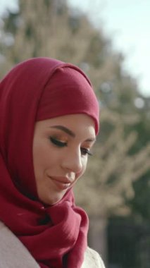 Canlı kırmızı tesettürlü bir kadın düşünceli bir şekilde uzaklara bakar, yumuşak, sıcak güneş ışığıyla yıkanır.