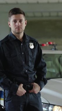 Standart polis üniforması giymiş bir adam emniyet teşkilatındaki rolünü göstermek için bir polis arabasının önünde güvenle duruyor.