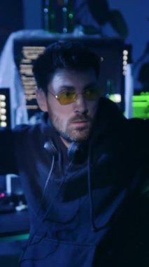 Kapüşonlu pelerinli bir figür loş bir odadaki bilgisayara sabitlenir. Diğeri, güneş gözlüğü ve kulaklıkla, ekranlarındaki verileri inceleyerek, teknolojik gerilimi artırıyor.