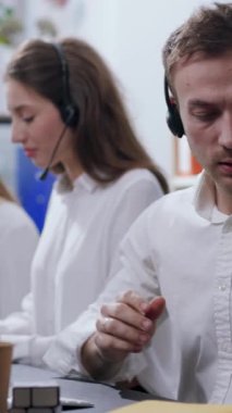 Genç bir adam, yoğun bir çağrı merkezinde çalışırken, çeşitli görevleri yerine getirirken gözle görülür bir şekilde stresli görünür.