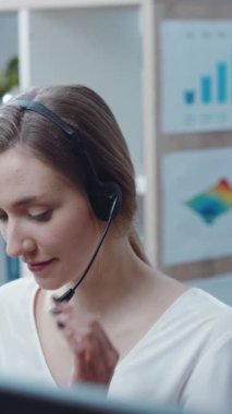 Odaklanmış, kendini işine adamış genç bir kadın, müşteri desteğinde üstün olduğu modern ofis ortamında bir kulaklık kullanıyor.