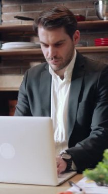 Şık giyinmiş odaklanmış profesyonel bir adam modern ofis ortamında özenle dizüstü bilgisayarı üzerinde çalışıyor.