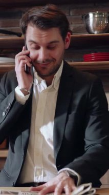 Terzi kıyafeti giymiş profesyonel bir adam sabah kahvesinin tadını çıkarırken şık bir mutfakta gazete okur.