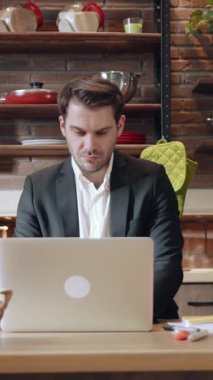 Modern iş hayatı dengesini gösteren şık bir mutfakta dizüstü bilgisayar kullanan odaklanmış bir adam..