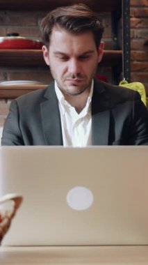 Konforlu bir kafede dizüstü bilgisayar üzerinde çalışan takım elbiseli bir profesyonel.