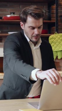 Profesyonel takım elbiseli bir adam dizüstü bilgisayarına, modern mutfak dekoruyla çevrili.