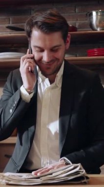 Takım elbiseli profesyonel bir adam, etrafı belgelerle çevrili şık bir ofis ortamında telefonla konuşur..