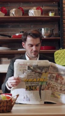 Takım elbiseli iyi giyimli bir adam şık bir mutfak masasında oturuyor, zarif bir dekorun ortasında gazete okumakla meşgul.