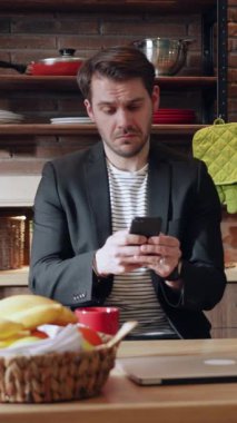 Şık, modern bir genç adam akıllı telefonunu rahat, davetkar bir mutfak alanında kullanmaya kendini kaptırmış.