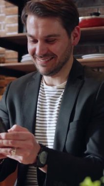 Neşeli bir adam modern bir kafede akıllı bir telefonla eğleniyor.