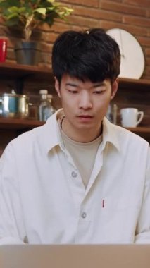 Genç bir adam, ışık ve konforla dolu sıcak, davetkar bir mutfakta otururken dikkatle dizüstü bilgisayarına odaklanır.