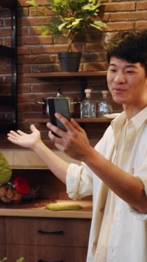 Neşeli genç bir adam neşeli bir şekilde şık ve bitkisel bir mutfakta sıcak bir selfie çekiyor.