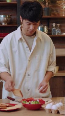 Genç bir adam şık bir mutfakta titizlikle taze malzemeler hazırlıyor. Yemek pişirme yeteneğini açıkça gösteriyor.