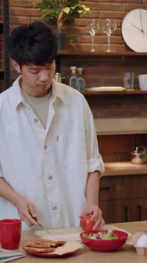 Şık bir mutfakta, odaklanmış genç bir adam titizlikle bir tabak ekmek ve taze salata hazırlıyor.