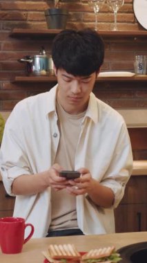 Tamamen akıllı telefonuna dalmış genç bir adam şık ve modern bir mutfakta lezzetli bir yemeğin tadını çıkarıyor.