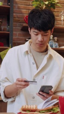 Mobil ödemelerle meşgul olan genç bir adam şık bir kafede yemeğin tadını çıkarıyor.