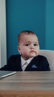 Şık bir takım elbise giymiş şık küçük bir çocuk modern ofis ortamında kameraya tuhaf bir şekilde bakıyor.