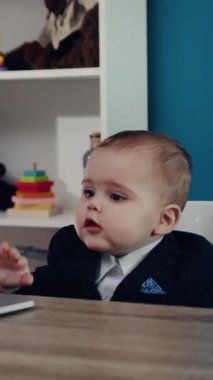 Şık, şık bir takım elbise giymiş odaklanmış ve kararlı bir bebek, modern bir çalışma alanında dizüstü bilgisayar keşfediyor.