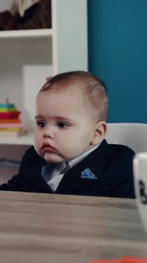 Kusursuz bir şekilde küçük bir takım elbise giymiş şık bir bebek, kendine güvenen bir şekilde bir masada oturuyor, ışık saçıyor.