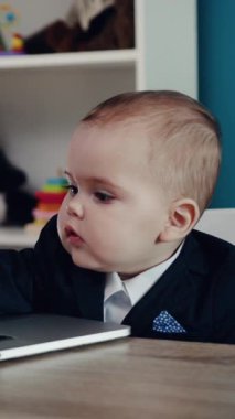 Şık takım elbiseli bir çocuk dizüstü bilgisayara odaklanır. Meraklarını ve zevklerini gösterir.