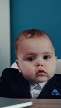 Özel dikim takım elbiseli küçük bir masada oturan masum ve meraklı bir çocuk.