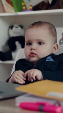 Çok düşünceli bir bebek, parlak, rahat bir yerde, renkli oyuncaklarla çevrili, açık bir dizüstü bilgisayara bakar.