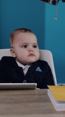 Akıllı bir takım elbise giyen odaklanmış genç bir çocuk, kendine güvenen bir şekilde bir masada oturuyor, tamamen kurumsal ciddiyeti somutlaştırıyor.