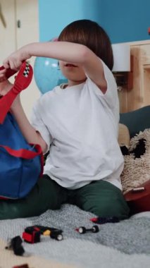 Genç bir çocuk renkli sırt çantasını dikkatlice ve neşeyle düzenliyor. Odaklanışını ve neşeli ruhunu sergiliyor.