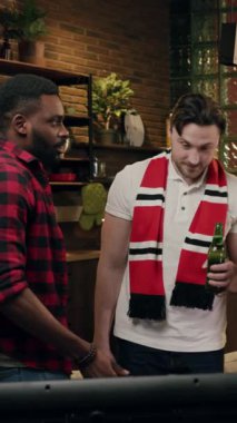 İki yakın arkadaş evde maç izlerken heyecan ve neşe dolu bir anı paylaşıyorlar.