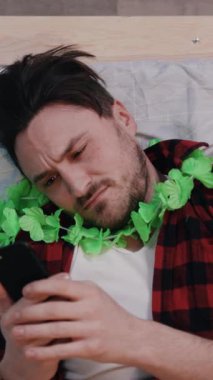 Renkli ekose gömlek ve canlı bir tropikal ley giyen sıradan giyinmiş bir adam akıllı telefonuna odaklanır.