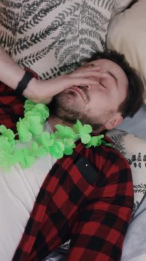 Bir adam rahat bir ortamda huzurlu bir şekilde uyur, kaygısız bir partinin renkli Hawaii yapraklarıyla süslenir.