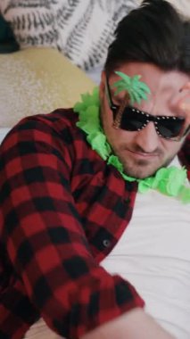 Şık bir güneş gözlüğü ve renkli bir çiçek kolyesi takmış, kaygısız bir yaz havası yayıyor.