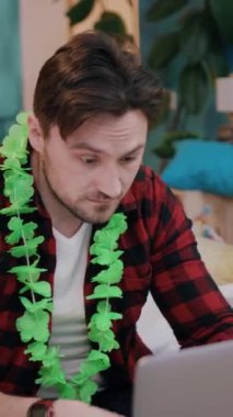 Parlak yeşil bir lei giyen genç bir adam odaklanmış ve yoğun bir şekilde bilgisayarının üzerinde çalışıyor.