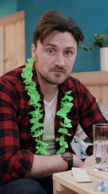 Bir adam eğlenceli bir toplantıdan mutlu bir şekilde zevk alır, renkli bir şenlik kolyesiyle süslenir, rahat bir havayı somutlaştırır.