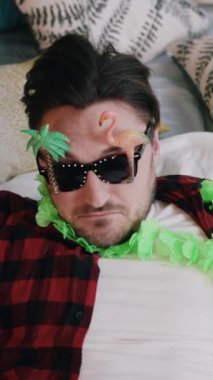 Renkli bir tropikal dekorun ortasında güneş gözlüğü takan bir kişinin yer aldığı neşeli ve canlı bir sahne resmedilir.