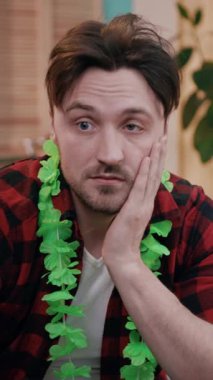 Yeşil bir çiçek kolyesi takan bir adam, şenlikli bir toplantıda sıkıntılı bir anı yakalıyor..