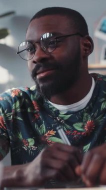 Renkli ve canlı bir gömlek içinde odaklanmış ve kararlı bir genç adam, parlak ve ilham verici bir çalışma alanına yazar.